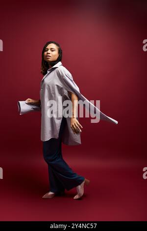 Une jeune femme à la mode avec des cheveux tressés met en valeur son style unique dans un cadre de studio vibrant. Banque D'Images