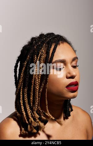 Une jeune femme présente sa coiffure tressée unique et ses lèvres rouges audacieuses dans un environnement de studio moderne. Banque D'Images