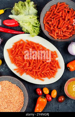 Pâtes végétaliennes non cuites ou macaronis, fusilli de lentilles rouges dans l'assiette. Banque D'Images