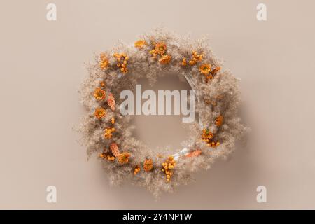 Couronne pour Thanksgiving Day avec des fleurs oranges et des matériaux naturels secs sur fond beige. Vue de dessus. Carte de vœux avec espace de copie. Banque D'Images