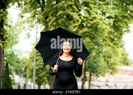 Une belle femme grande taille marche joyeusement avec son parapluie au milieu du feuillage coloré d'automne dans un parc pittoresque. Banque D'Images