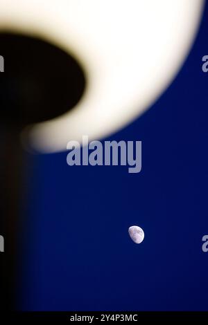 Un lampadaire est illuminé tandis que le croissant de lune brille dans le ciel bleu foncé, créant une atmosphère nocturne tranquille. Banque D'Images