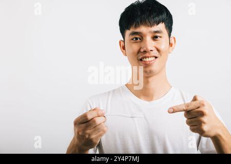 L'homme asiatique se brosse les dents le matin, tient une brosse à dents, sourit et pointe Banque D'Images