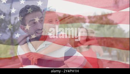 Image du drapeau américain au-dessus des parents caucasiens heureux portant le fils et la fille dans le jardin ensoleillé Banque D'Images