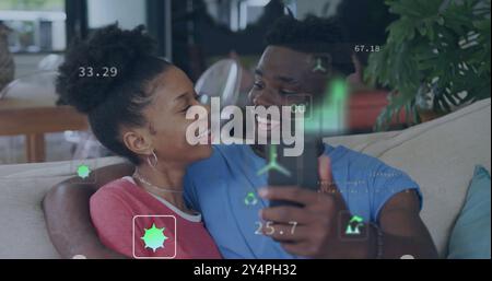 Image d'icônes écologiques et de traitement de données sur un couple afro-américain heureux utilisant smarthopne Banque D'Images