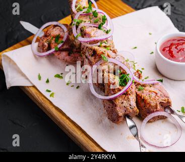 Kebabs juteux de porc sur des brochettes disposées sur une planche décorative Banque D'Images