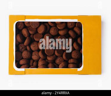 Vue de dessus d'une boîte jaune ouverte remplie de biscuits ronds au chocolat sur fond blanc Banque D'Images