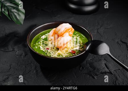 Présentation gourmande de soupe de crevettes aux épinards ornée de garnitures dans un bol sombre sur une surface texturée Banque D'Images