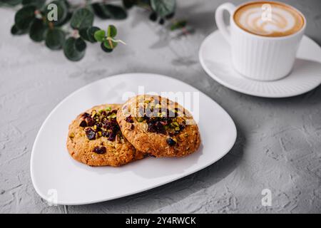 Biscuits artisanaux aux aux pistaches sur une assiette à côté d'une tasse à cappuccino, eucalyptus en arrière-plan Banque D'Images