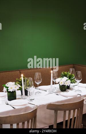 Table à manger confortable avec bougies allumées, fleurs fraîches et verrerie élégante sur fond vert Banque D'Images