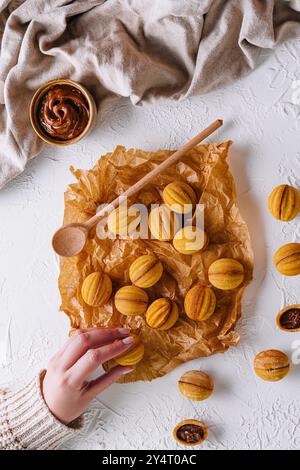 Coup de tête d'une main atteignant des biscuits fraîchement cuits en forme de noix avec du caramel Banque D'Images