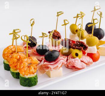 Plateau de hors-d'œuvre gastronomique exquis avec un assortiment élégant de fromages. Crevettes. Olives. Salami. Concombre. Raisin. Et tomate séchée au soleil. PE Banque D'Images