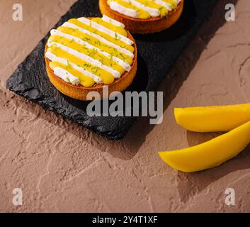 Trois délicieuses tartes à la mangue avec garniture crémeuse et zeste de citron vert, élégamment servies sur une planche en ardoise Banque D'Images