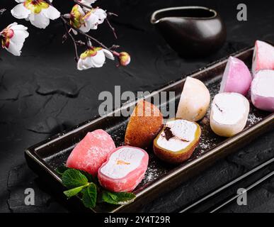 Sélection japonaise de crème glacée mochi servie dans un plateau en céramique avec des fleurs de cerisier, esthétique sombre Banque D'Images