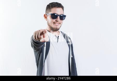 Beau gars dans des lunettes de soleil souriant et pointant vers la caméra isolé Banque D'Images