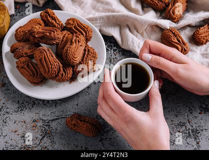 Mains tenant une tasse de café à côté d'une assiette de biscuits au chocolat sur une table rustique Banque D'Images