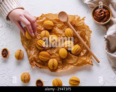 Coup de tête d'une main atteignant des biscuits fraîchement cuits en forme de noix avec du caramel Banque D'Images