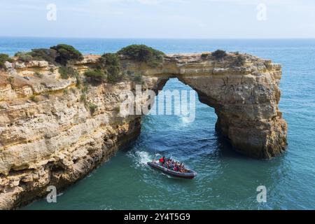 Un bateau avec des touristes navigue à travers une arche rocheuse naturelle au-dessus de la mer bleue claire, Arco de Albandeira, Lagoa, Algarve, Portugal, Europe Banque D'Images