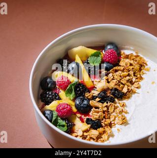 Bol sain de yaourt avec granola et fruits mélangés, présenté sur un fond brun élégant avec des ombres Banque D'Images