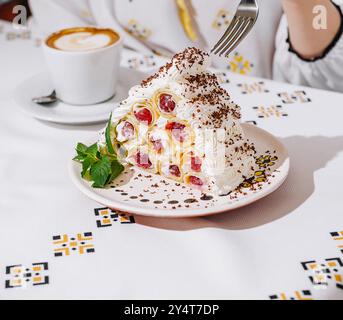 Gros plan de la main d'une femme prenant un morceau de gâteau à la crème de fruits, avec un cappuccino sur la table Banque D'Images