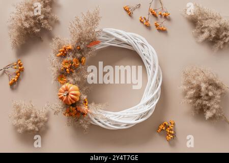 Couronne avec des fleurs oranges et des matériaux naturels secs sur fond beige. Vue de dessus. Atelier pour la décoration de jour de Thanksgiving faite à la main. Banque D'Images