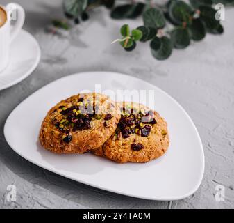 Biscuits artisanaux aux aux pistaches sur une assiette à côté d'une tasse à cappuccino, eucalyptus en arrière-plan Banque D'Images