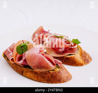 Bruschetta gourmande au prosciutto et au basilic sur une assiette propre sur fond blanc Banque D'Images