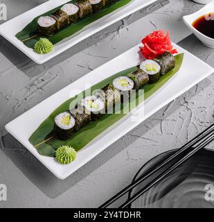 Présentation élégante de rouleaux de sushi à l'avocat garnis de wasabi et de gingembre sur des assiettes modernes, prêtes à servir Banque D'Images