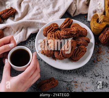 Mains tenant une tasse de café à côté d'une assiette de biscuits au chocolat sur une table rustique Banque D'Images