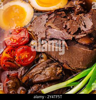 Ramen de boeuf traditionnel avec oeuf à la coque, tomates et oignons verts dans un bouillon riche Banque D'Images
