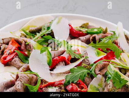 Carpaccio de boeuf en tranches orné de copeaux de parmesan, de roquette et de poivrons rouges Banque D'Images