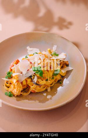 Service élégant de pâtes tagliatelles avec crevettes, champignons et copeaux de parmesan garni d'herbes fraîches Banque D'Images