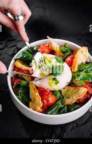 Bol de salade de fromage burrata, avec tomates mûres, épinards et pain croustillant sur fond noir Banque D'Images