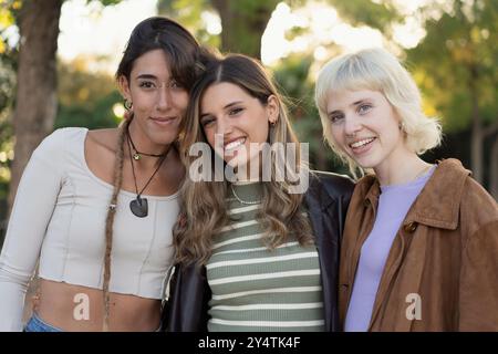 Portrait de trois jeunes amies diverses souriant ensemble dans un parc. Groupe multiethnique montrant l'unité, l'amitié et le style individuel. Concep Banque D'Images