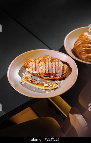 Deux assiettes avec de délicieux croissants frais appétissants avec des tranches de banane et des flocons d'amandes sont couchées sur une table Banque D'Images