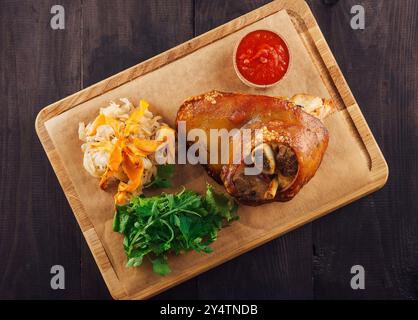 Le jarret de porc croustillant est servi sur une planche de bois avec de la salade, de la choucroute et de la sauce Banque D'Images