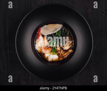 Soupe miso aromatique avec tofu, algues wakame, champignons shiitake et fruits de mer servis dans un bol noir Banque D'Images