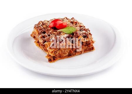 La portion carrée de lasagne recouverte d'une feuille de basilic et de tranches de tomates est assise sur une assiette blanche Banque D'Images