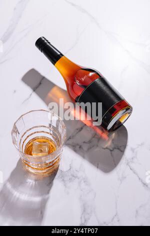 Bouteille de liqueur jette une ombre près d'un verre de roches avec de la glace sur un comptoir de marbre Banque D'Images