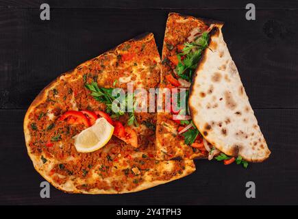 Pain plat turc lahmacun avec viande hachée, tomates, persil, épices servies avec citron sur une table en bois foncé Banque D'Images