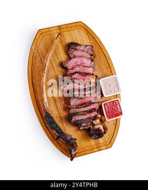 Steak tomahawk grillé tranché couché sur une planche de bois avec deux sauces Banque D'Images