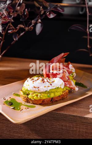 Toast avec de la purée d'avocat et oeuf poché décoré de prosciutto et de graines, arrosé d'huile d'olive Banque D'Images