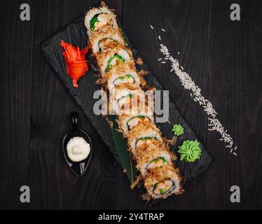 Délicieux rouleau de sushi tempura avec poisson et avocat servi sur un plateau d'ardoise noire avec gingembre, wasabi et riz dispersé Banque D'Images