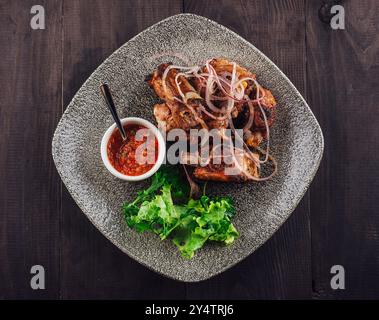 Côtes de porc grillées avec oignons rouges et herbes servies sur une assiette avec sauce et laitue fraîche sur fond de bois foncé Banque D'Images