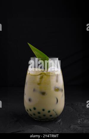 Verre de latte matcha glacé avec perles de tapioca est garni d'une feuille de palmier, créant une boisson rafraîchissante et exotique Banque D'Images