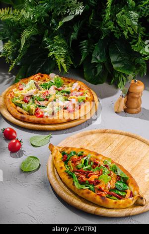 Pizza salade César et pide turque avec tomates séchées au soleil et épinards couchés sur des planches de bois sur une table grise Banque D'Images