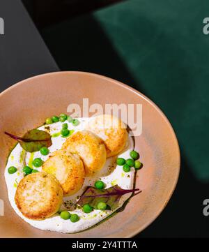 Côtelettes de poulet avec petits pois verts et sauce blanche couchées dans une assiette beige sur une table sombre Banque D'Images