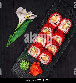 Assiette en ardoise noire avec une portion de rouleaux de sushi uramaki californiens décorés de caviar tobiko rouge, servis avec gingembre, wasabi et sauce soja sur noir Banque D'Images