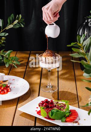 Personne arrosant la sauce sur la crème glacée parmi une sélection de desserts élégants assortis Banque D'Images