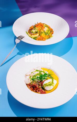 Deux plats exquis sont servis sur des assiettes blanches, mettant en valeur un arrangement vibrant de couleurs et de textures sur un fond bleu et violet vif Banque D'Images